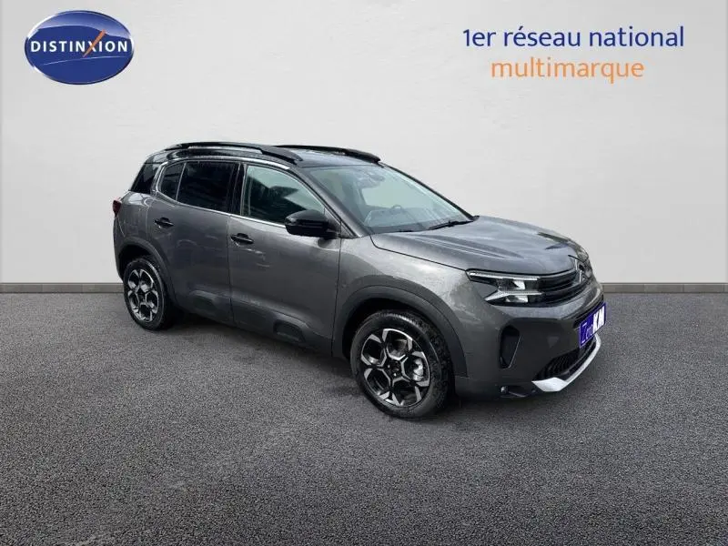 Vue 3/4 avant droit du Citroën C5 Aircross gris Platinium avec barres de toit et jantes alu distinctives.