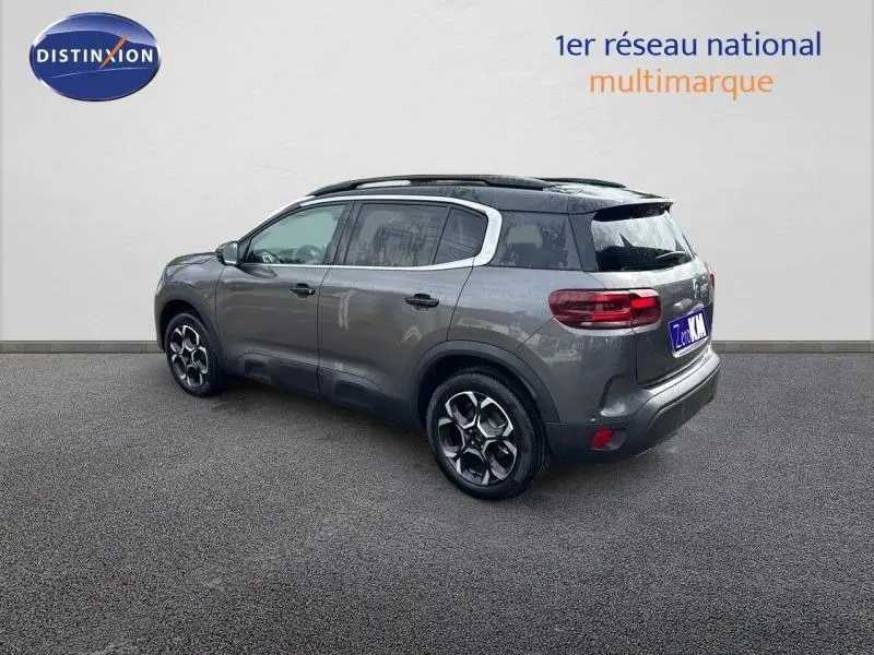 Vue 3/4 arrière droite d'un Citroën C5 Aircross gris Platinium avec barres de toit et jantes alu distinctives.