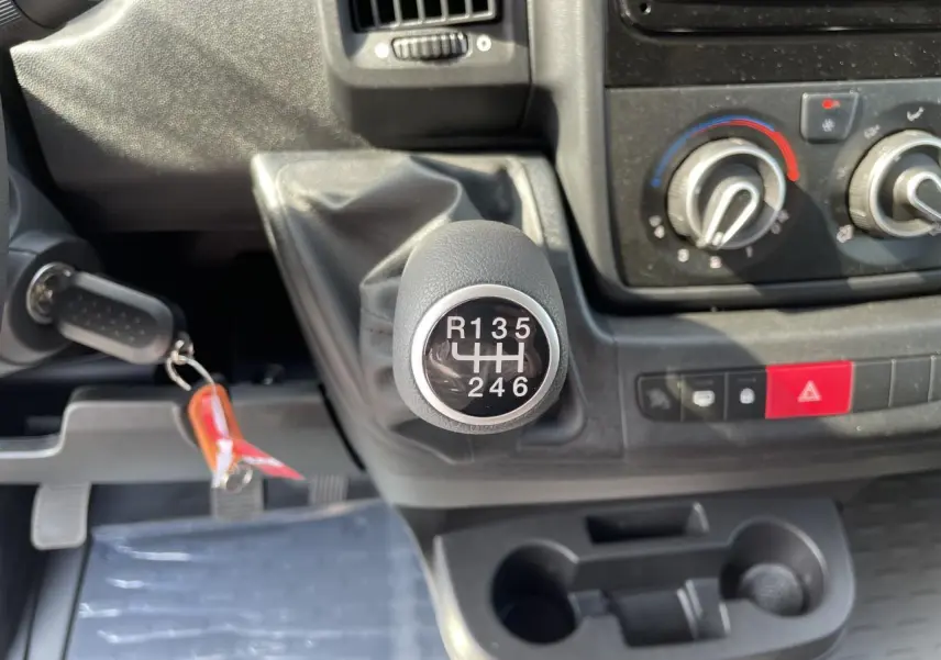 Gros plan sur le levier de vitesse manuel du Peugeot Boxer Fourgon blanc, avec commandes de climatisation et porte-gobelets visibles.