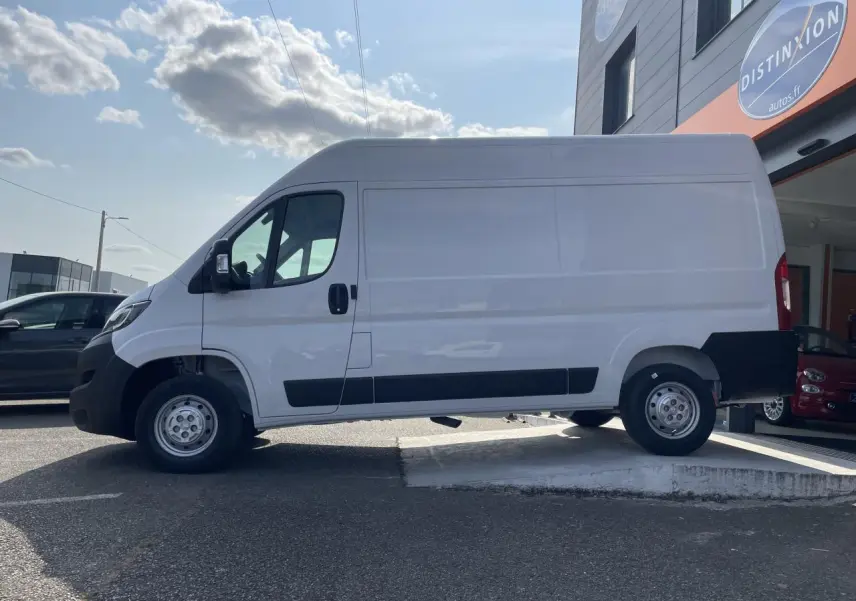 Profil droit du Peugeot Boxer Fourgon blanc 2023 avec porte latérale coulissante et protections noires sur parking.
