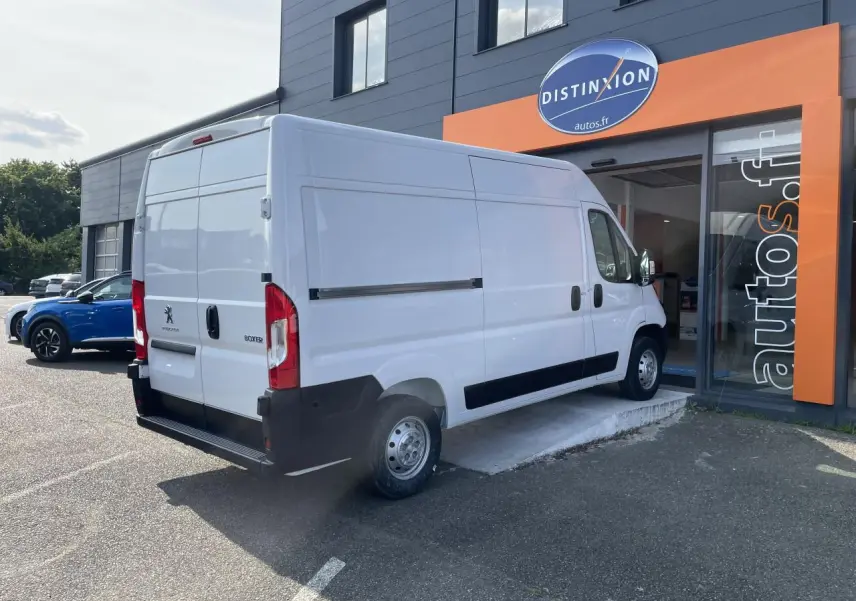Vue 3/4 arrière droite d'un utilitaire Peugeot Boxer Fourgon blanc garé devant un bâtiment commercial.