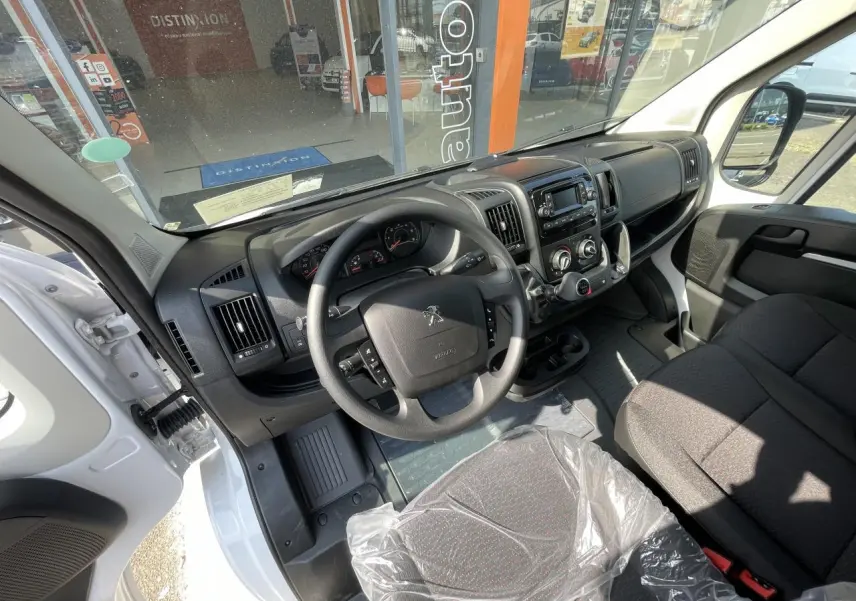 Vue intérieure côté conducteur du Peugeot Boxer Fourgon blanc 2023, tableau de bord et volant visibles.