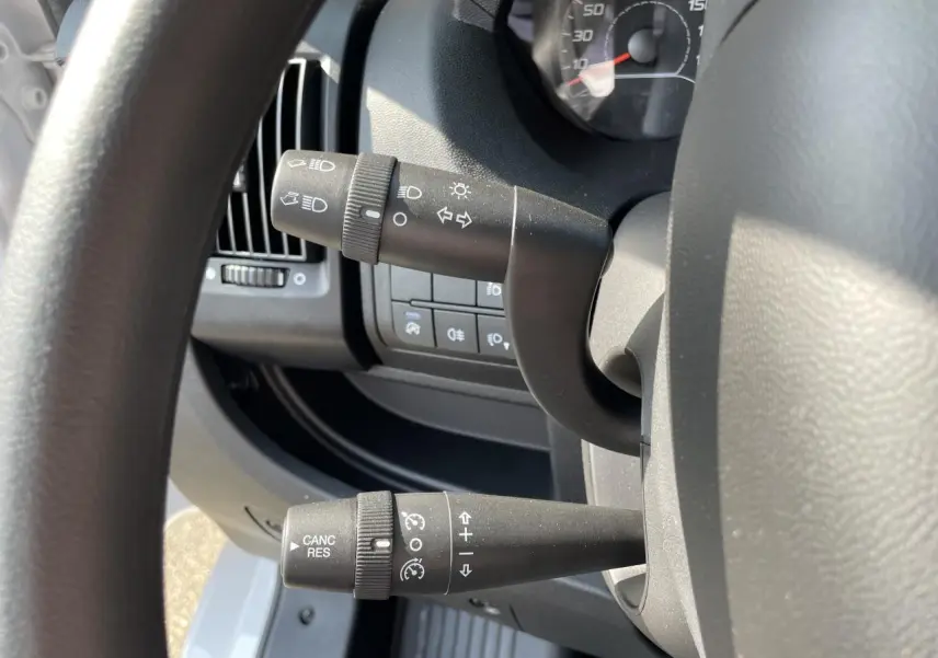 Gros plan sur les commandes de clignotants et régulateur de vitesse du Peugeot Boxer Fourgon blanc, côté gauche du volant.