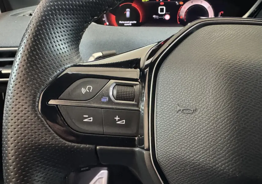 Gros plan sur le volant cuir noir perforé côté gauche du Peugeot 3008 2021 avec commandes audio et tableau de bord digital.