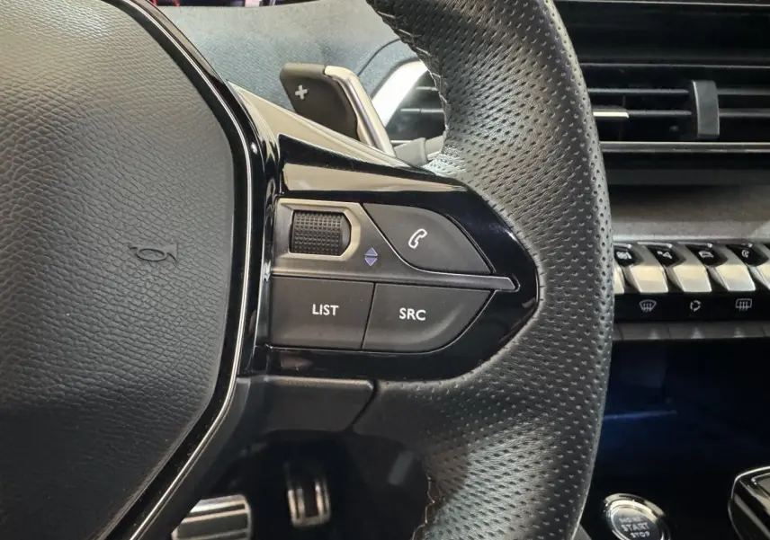 Gros plan sur le côté gauche du volant cuir perforé du Peugeot 3008 gris clair, avec commandes audio et tableau de bord en arrière-plan.