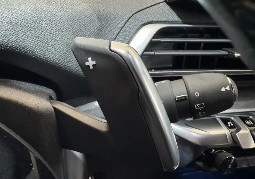 Gros plan sur la palette de changement de vitesse droite en plastique noir et chrome dans l’habitacle d’un Peugeot 3008 gris clair.