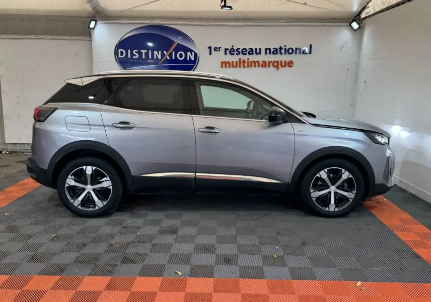 Vue latérale droite d’un Peugeot 3008 GT gris clair avec jantes alliage et toit noir dans un garage.