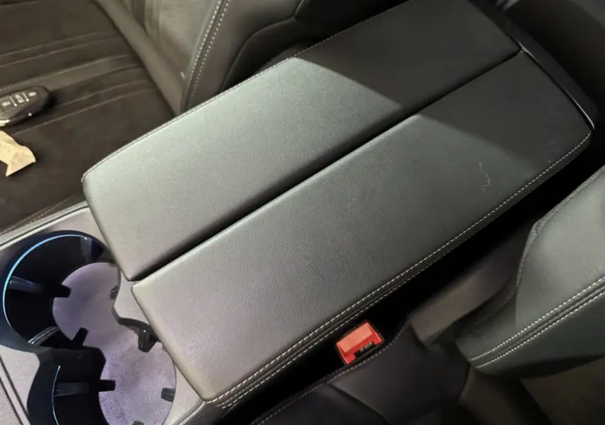 Vue rapprochée de l'accoudoir central en cuir noir avec surpiqûres blanches dans l'habitacle du Peugeot 3008 gris clair.