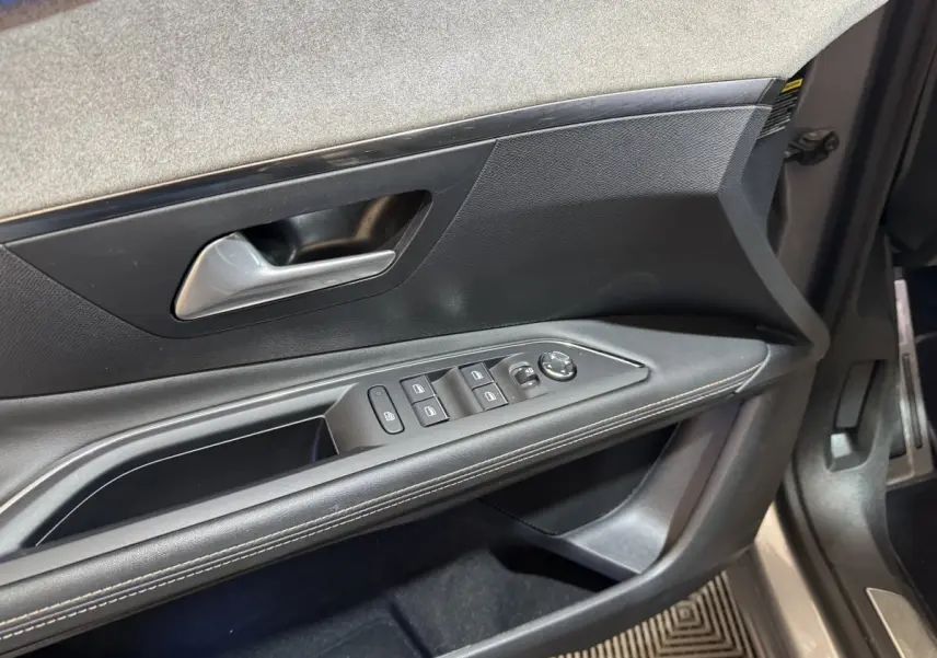 Vue rapprochée de la porte avant gauche du Peugeot 3008 gris clair, montrant les commandes des vitres et le revêtement noir avec surpiqûres.