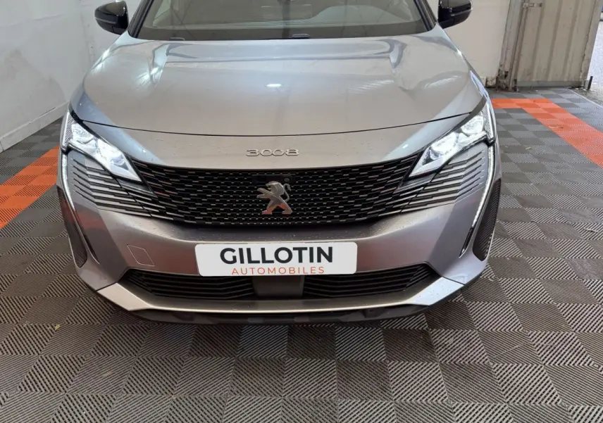 Vue avant d'une Peugeot 3008 gris clair avec calandre noire et phares LED allumés dans un garage.