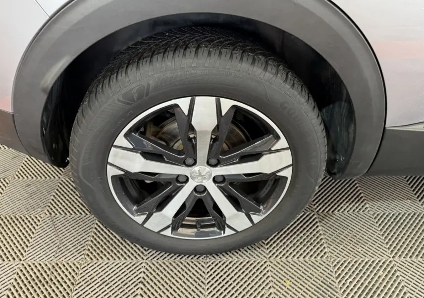 Gros plan sur la roue avant gauche d’un Peugeot 3008 gris clair, avec jante alliage bicolore noire et argentée.
