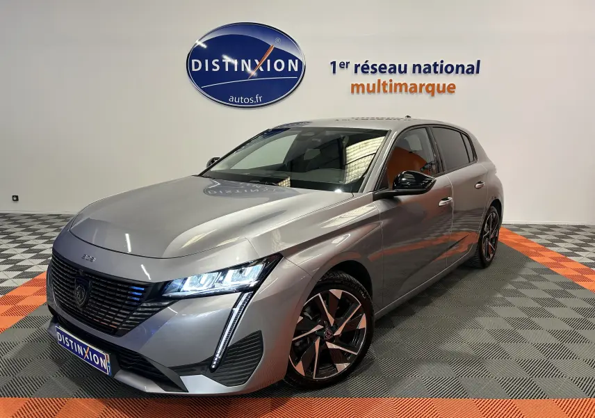Peugeot 308 gris en 3/4 avant droit, phares LED allumés et jantes alliage distinctives, en showroom.