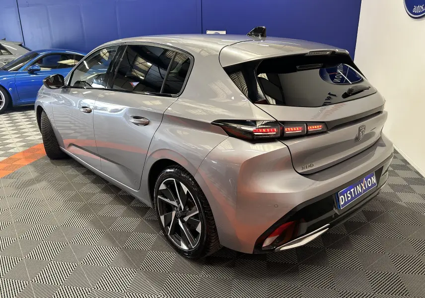 Peugeot 308 gris vue 3/4 arrière droit, feux arrière allumés, jantes alliage noires et toit avec antenne shark.