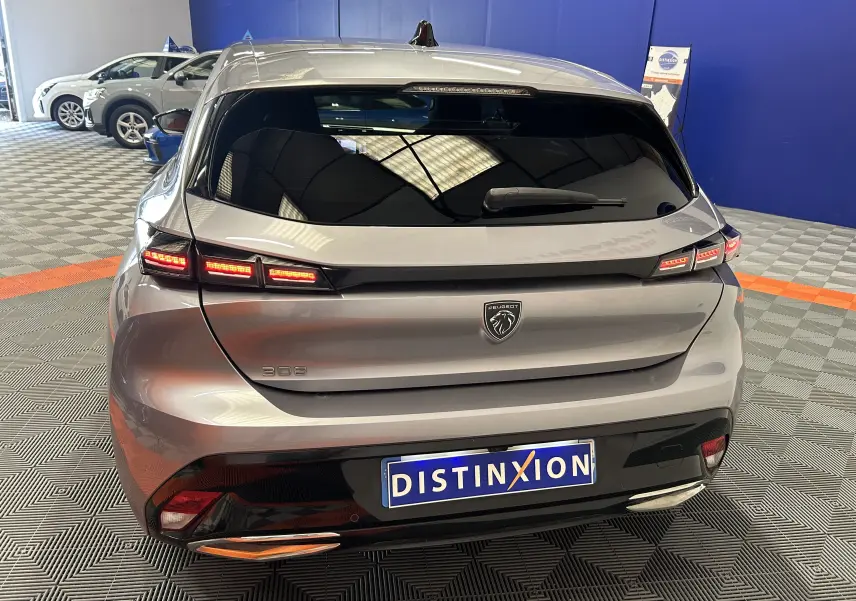 Vue arrière d'une Peugeot 308 gris métallisé avec feux LED allumés dans un showroom au sol damier.