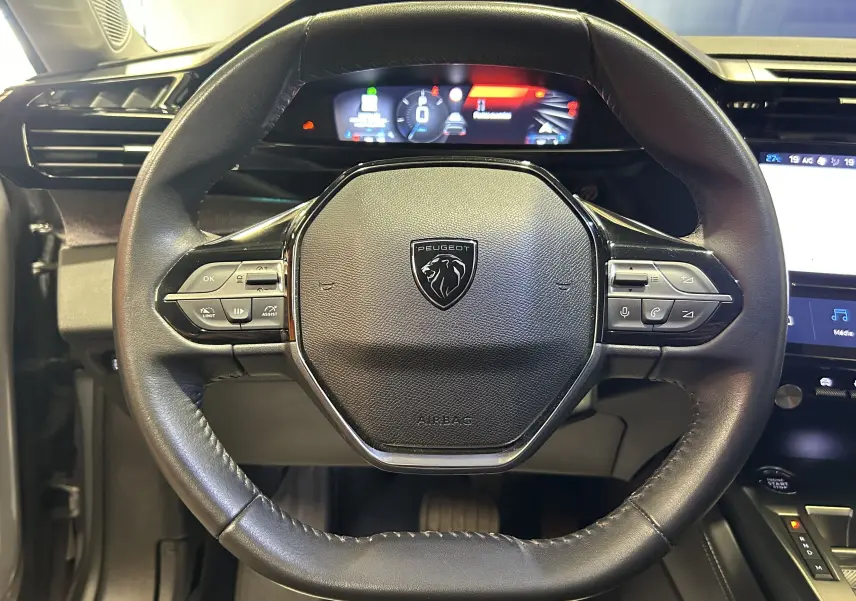 Vue rapprochée du volant noir de la Peugeot 308 2022 avec commandes intégrées et tableau de bord numérique en arrière-plan.