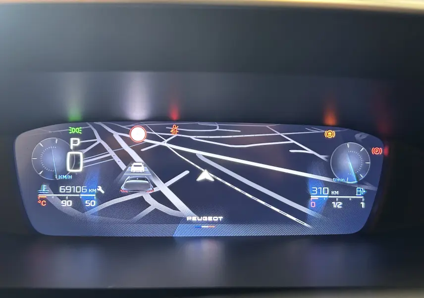 Tableau de bord numérique de Peugeot 308 gris, affichant la navigation GPS et les indicateurs de vitesse et carburant.