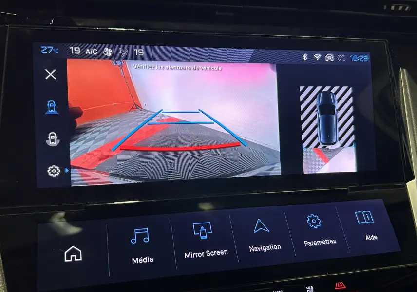 Écran de caméra de recul affichant l’arrière d’une Peugeot 308 gris avec lignes de guidage et vue 360° du véhicule.