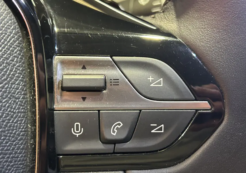Gros plan sur les commandes au volant côté gauche d’une Peugeot 308 gris, boutons de volume et téléphone visibles.