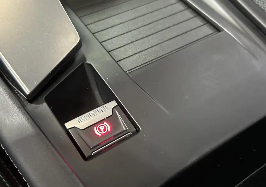 Gros plan sur le bouton de frein à main électronique rouge dans la console centrale noire d’une Peugeot 308 gris 2022.