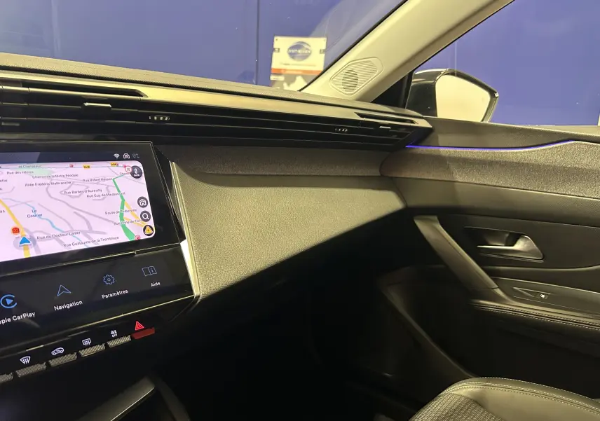 Vue intérieure côté passager de la Peugeot 308 gris, avec écran tactile GPS et éclairage d’ambiance bleu.