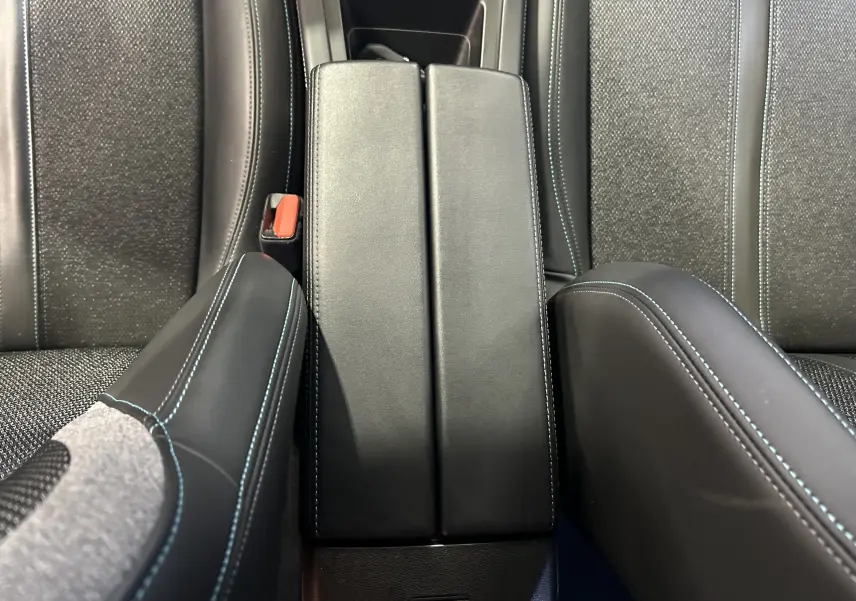 Gros plan sur l'accoudoir central en cuir noir avec surpiqûres bleues, entre les sièges arrière gris tissu de la Peugeot 308.