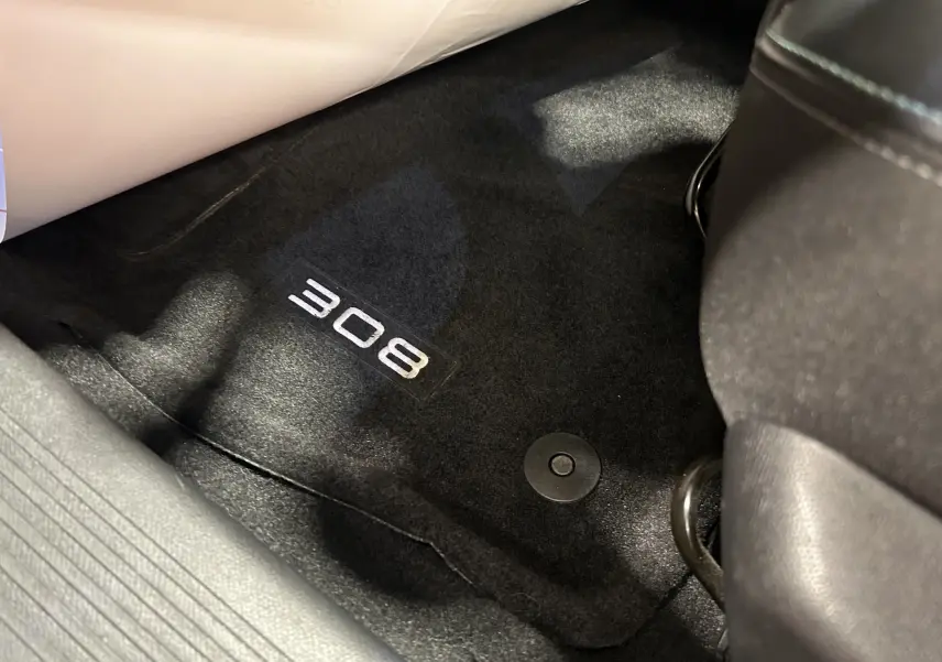 Détail du tapis de sol noir avec logo "308" visible côté passager avant d'une Peugeot 308 gris 2022.