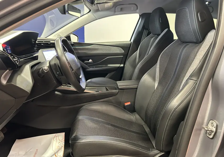 Vue intérieure côté conducteur de la Peugeot 308 gris, mettant en valeur les sièges en cuir et tissu avec surpiqûres bleues.