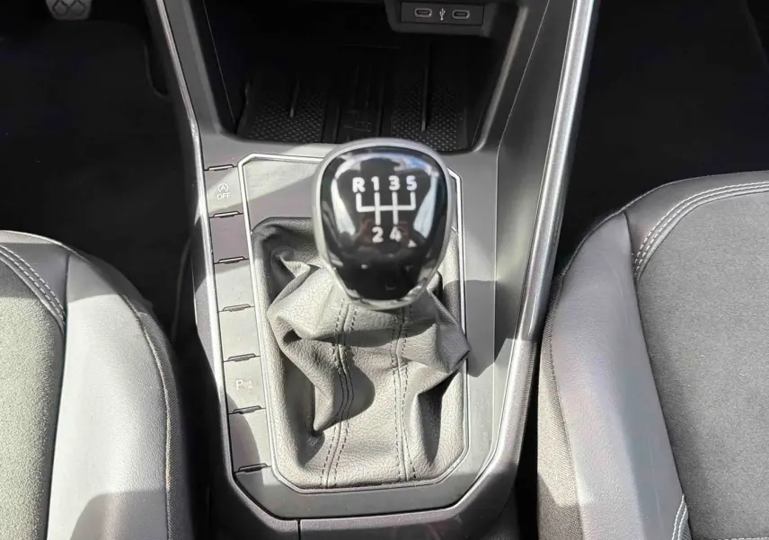 Vue rapprochée de la commande de boîte manuelle noire entourée de sièges en cuir gris dans une Volkswagen Polo 2025.