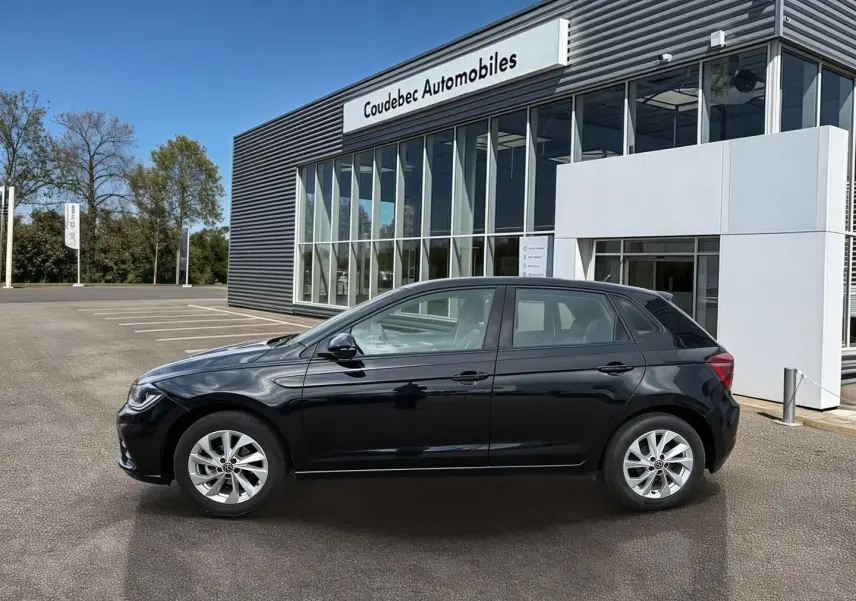Vue de profil côté gauche d'une Volkswagen Polo noire 2025 garée devant un bâtiment de concession.