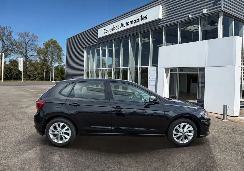 Profil latéral droit d'une Volkswagen Polo noire 2025 stationnée devant un bâtiment vitré de concession.