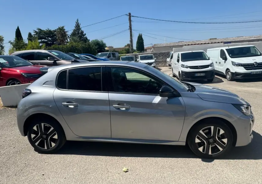 Profil côté gauche d'une Peugeot 208 Hybrid 110 gris métallisé avec jantes alliage 16 pouces, en extérieur parking.