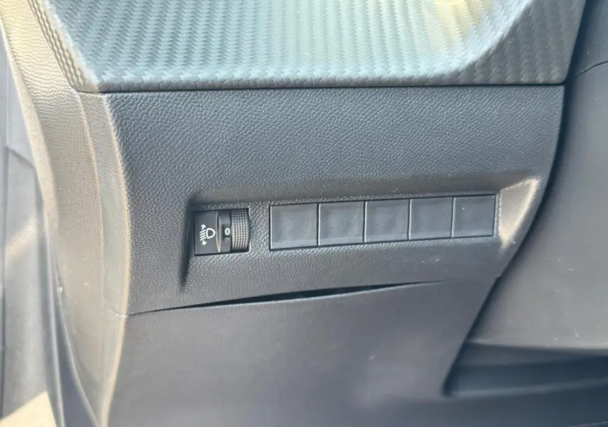 Détail du tableau de bord côté gauche d’une Peugeot 208 gris, montrant le réglage des phares.
