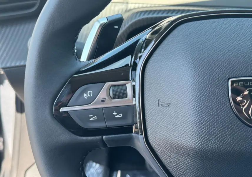 Gros plan sur le volant noir de la Peugeot 208 Hybrid 110 e-DCS6 Allure avec commandes intégrées côté gauche.