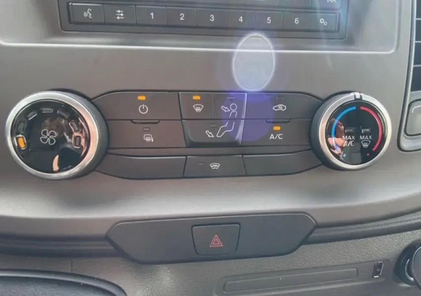 Gros plan sur les commandes de climatisation manuelle du Ford Transit Fourgon blanc 2023 avec boutons éclairés.