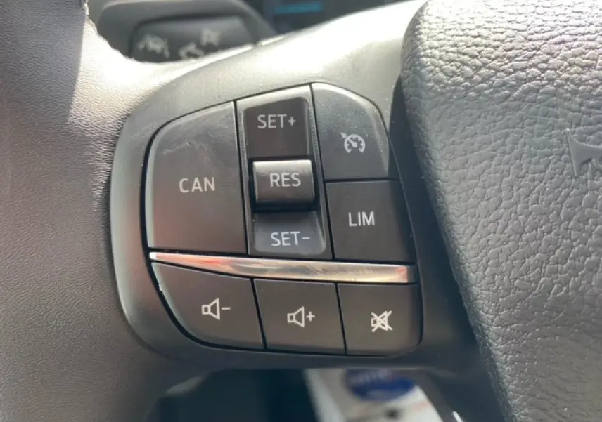 Gros plan sur les commandes du régulateur de vitesse et du volume audio sur le volant noir du Ford Transit Fourgon blanc 2023.