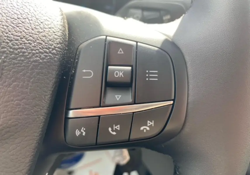 Gros plan sur les commandes multifonctions à gauche du volant du Ford Transit Fourgon blanc 2023.