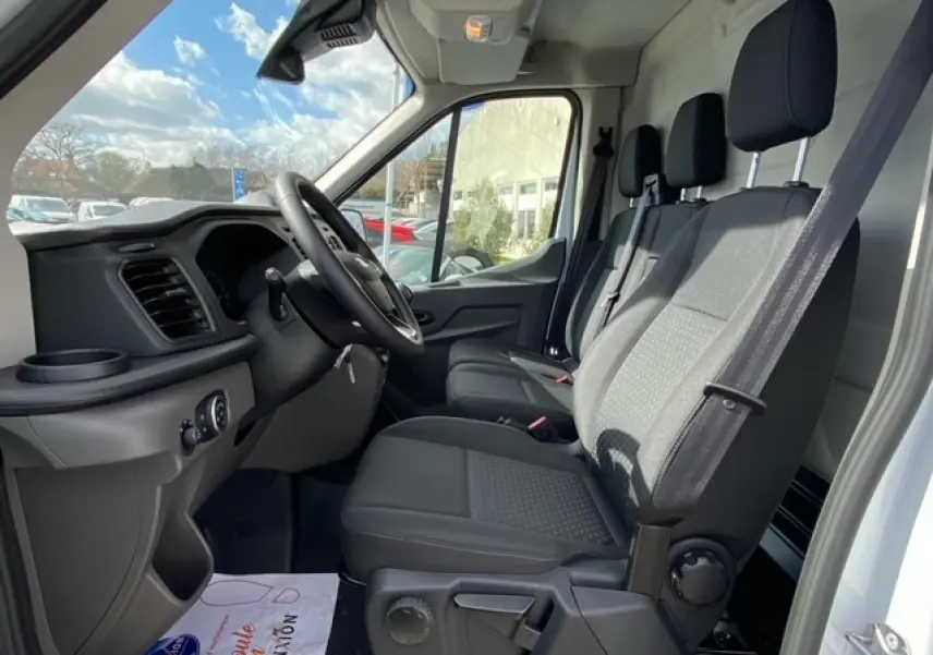Vue intérieure côté conducteur du Ford Transit Fourgon blanc 2023, montrant les sièges avant et le tableau de bord noir.