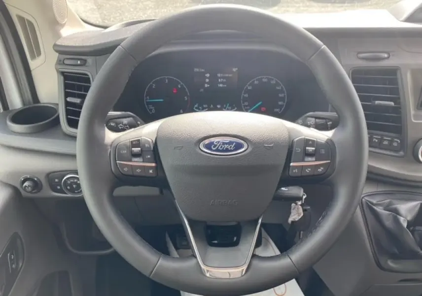 Vue rapprochée du volant multifonction du Ford Transit Fourgon 2023 avec tableau de bord et levier de vitesses visibles.