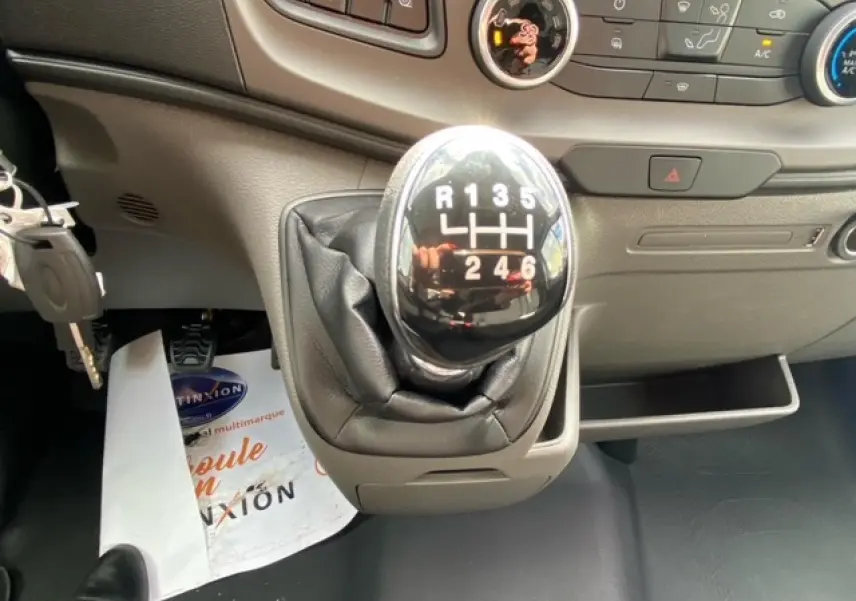 Le levier de vitesses manuel noir du Ford Transit Fourgon 2023, avec tableau de bord gris en arrière-plan.