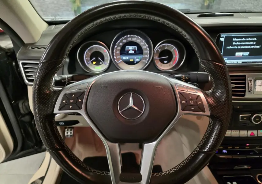 Vue rapprochée du volant en cuir noir perforé de la Mercedes Classe E Cabriolet 2014 avec tableau de bord et écran multimédia.