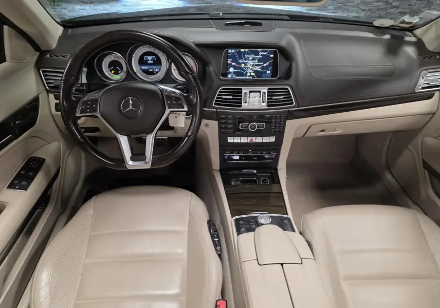 Vue intérieure avant de la Mercedes Classe E Cabriolet 2014 avec tableau de bord noir et sièges en cuir beige.