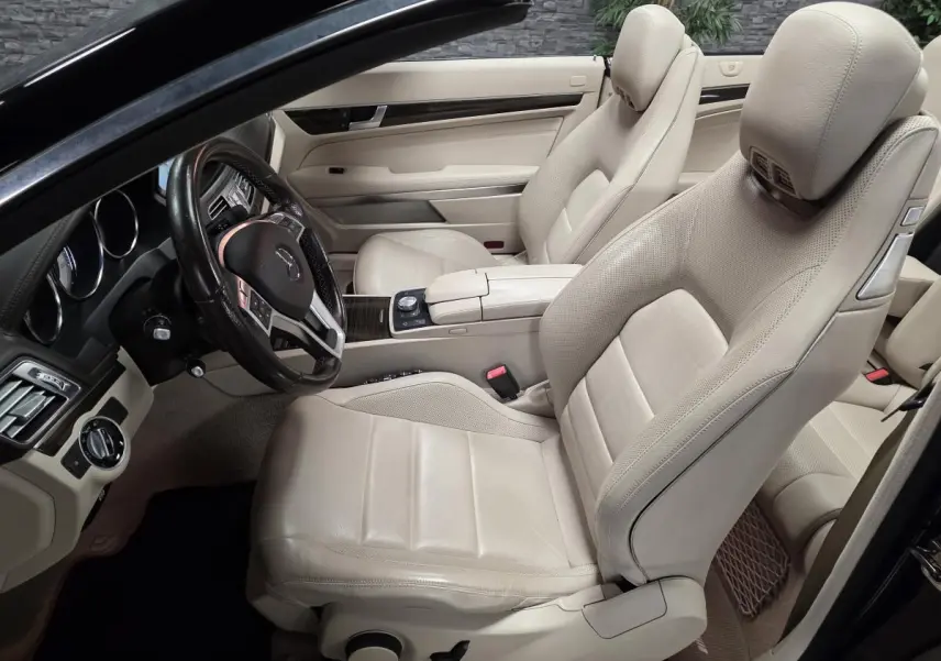 Intérieur beige clair d'une Mercedes Classe E Cabriolet 2014, vue côté conducteur avec sièges en cuir et volant multifonctions.