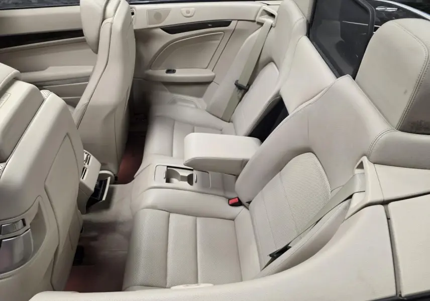 Vue intérieure arrière côté droit d'un cabriolet Mercedes Classe E 250 CDI noir avec sièges en cuir beige et accoudoir central relevé.