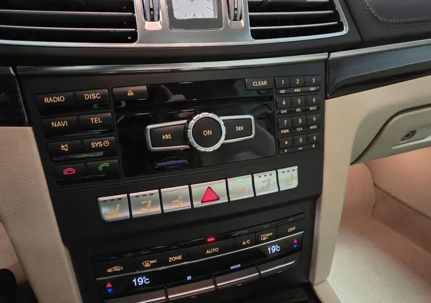 Console centrale beige et noire de la Mercedes Classe E Cabriolet 2014 avec commandes multimédia et climatisation automatique affichant 19°C