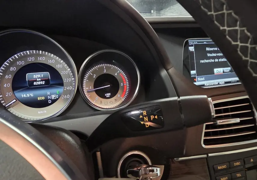 Tableau de bord et levier de boîte automatique d'une Mercedes Classe E Cabriolet noire, affichage numérique et écran multimédia visibles.