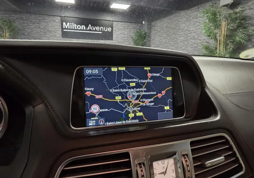 Vue rapprochée de la console centrale cuir noir avec écran GPS et horloge analogique Mercedes-Benz intégrée.