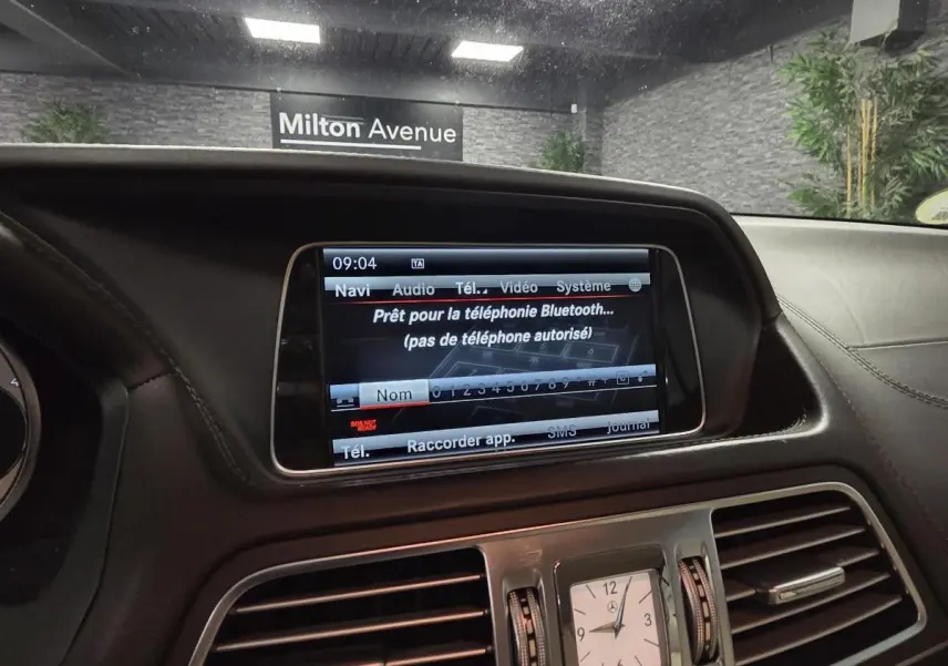 Vue intérieure du tableau de bord cuir noir de la Mercedes Classe E Cabriolet avec écran multimédia et horloge analogique centrale.