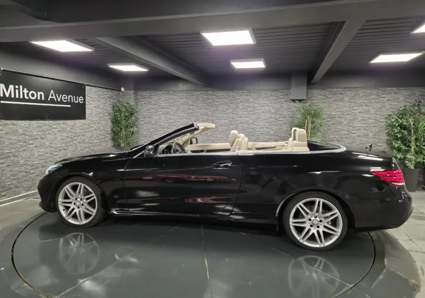 Profil droit d'une Mercedes Classe E Cabriolet noire avec intérieur cuir beige et jantes AMG 19 pouces en showroom.