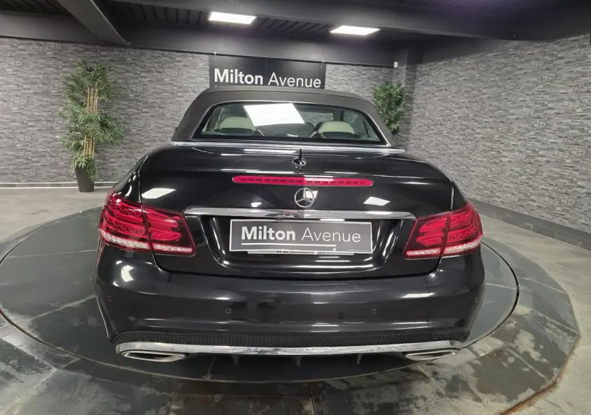 Vue arrière d'un cabriolet Mercedes Classe E noir avec double sortie d'échappement et feux arrière LED allumés.