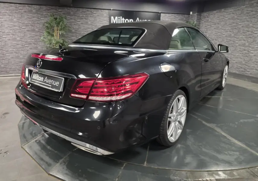 Vue 3/4 arrière droite d'une Mercedes Classe E Cabriolet noire avec capote fermée et jantes alliage AMG 19 pouces.
